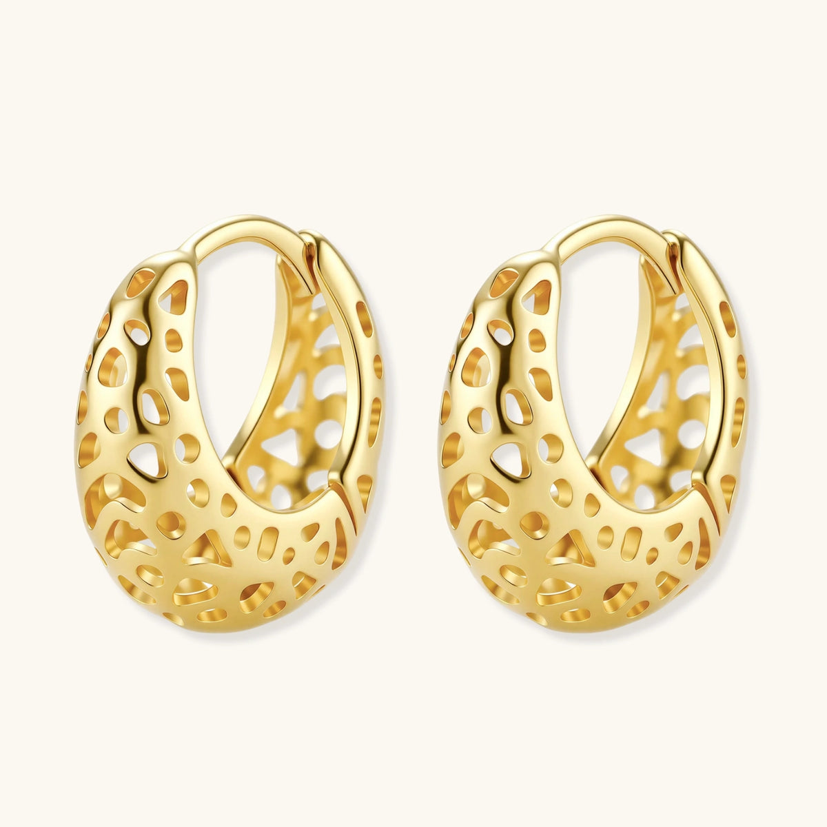 Close-up of small gold-plated hoop earrings with intricate honeycomb cutout pattern on cream background.