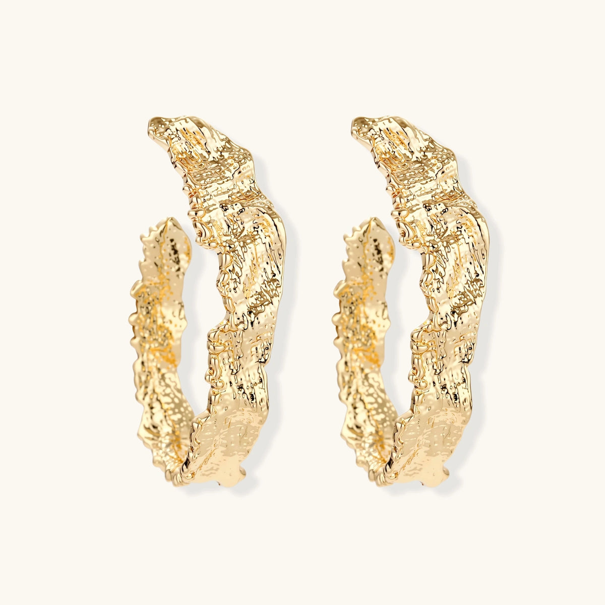 Close-up of sculptural hoop earrings with organic molten texture in silver and gold finishes on white background