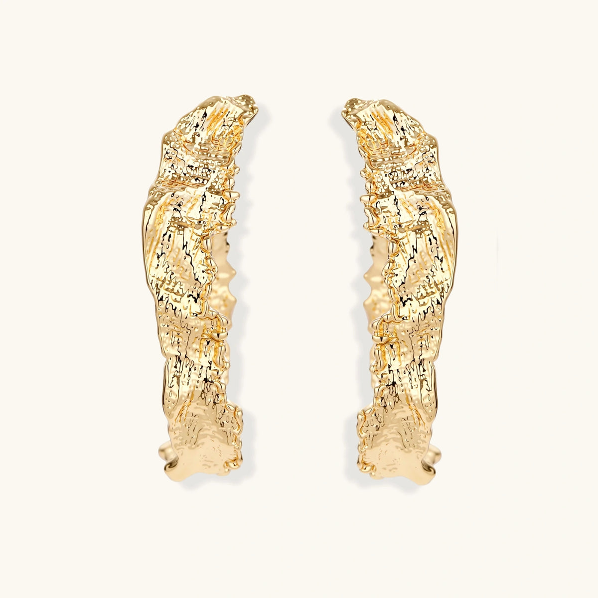 Close-up of sculptural hoop earrings with organic molten texture in silver and gold finishes on white background